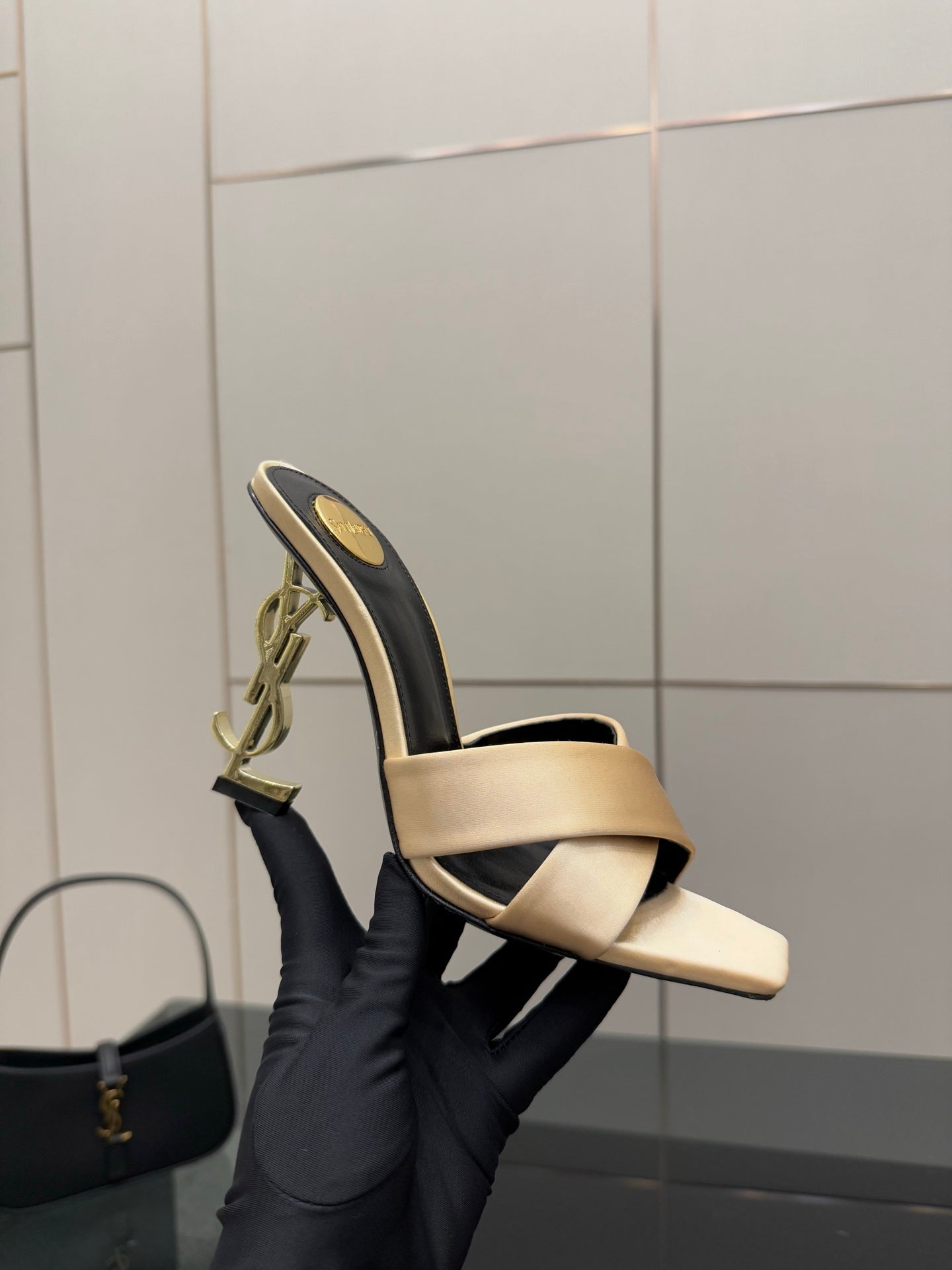 Cream heeled mule sandal held in hand, dark outer edge and gold YSL logo on heel.