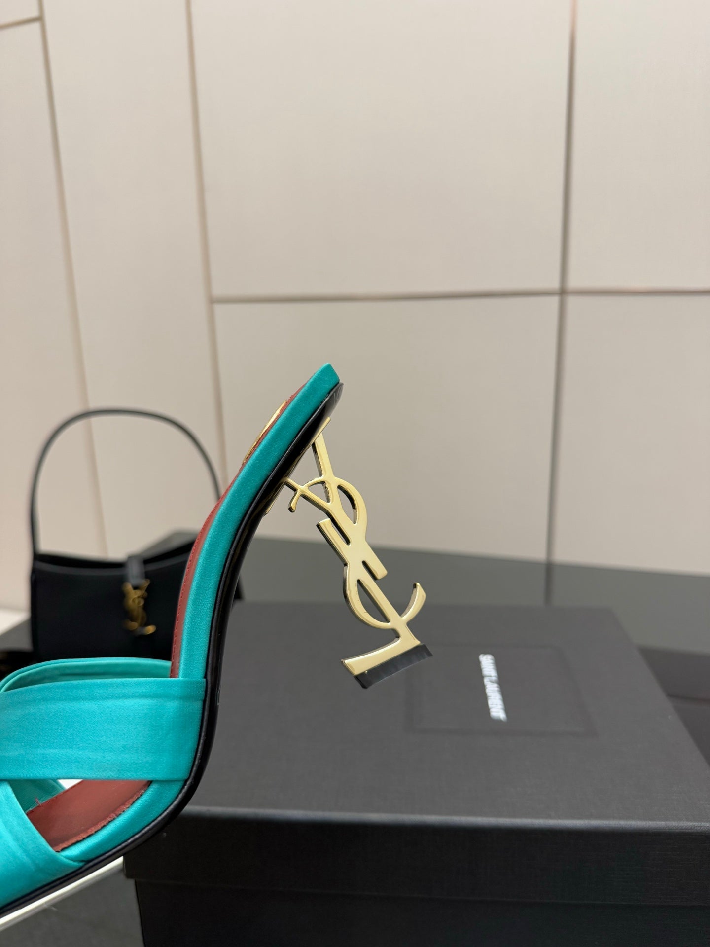 Close-up of teal YSL mule heel with gold logo ornament and red inner edge