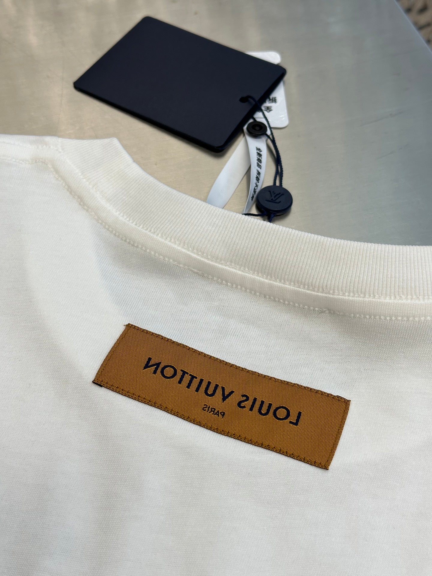 White T-shirt hem tag detail with brown Louis Vuitton label on neck area