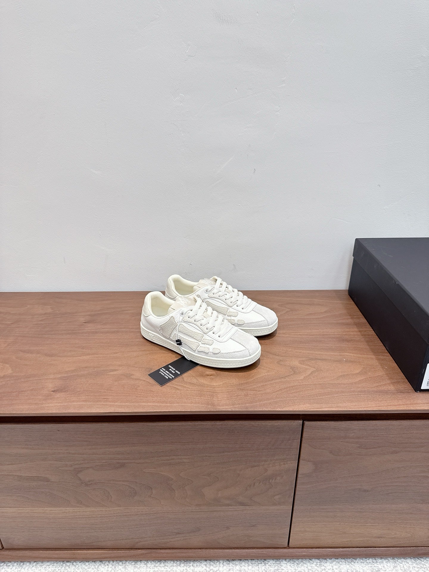 White lace-up sneakers, one pair side-by-side on a shelf with tag