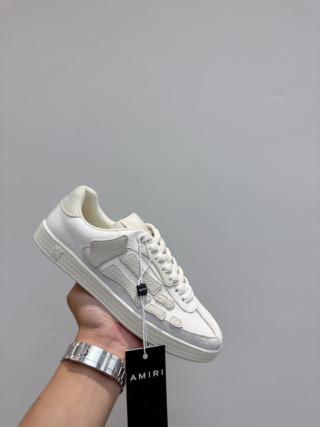 White low-top sneakers in hand, showing lace-up and side stripe detail