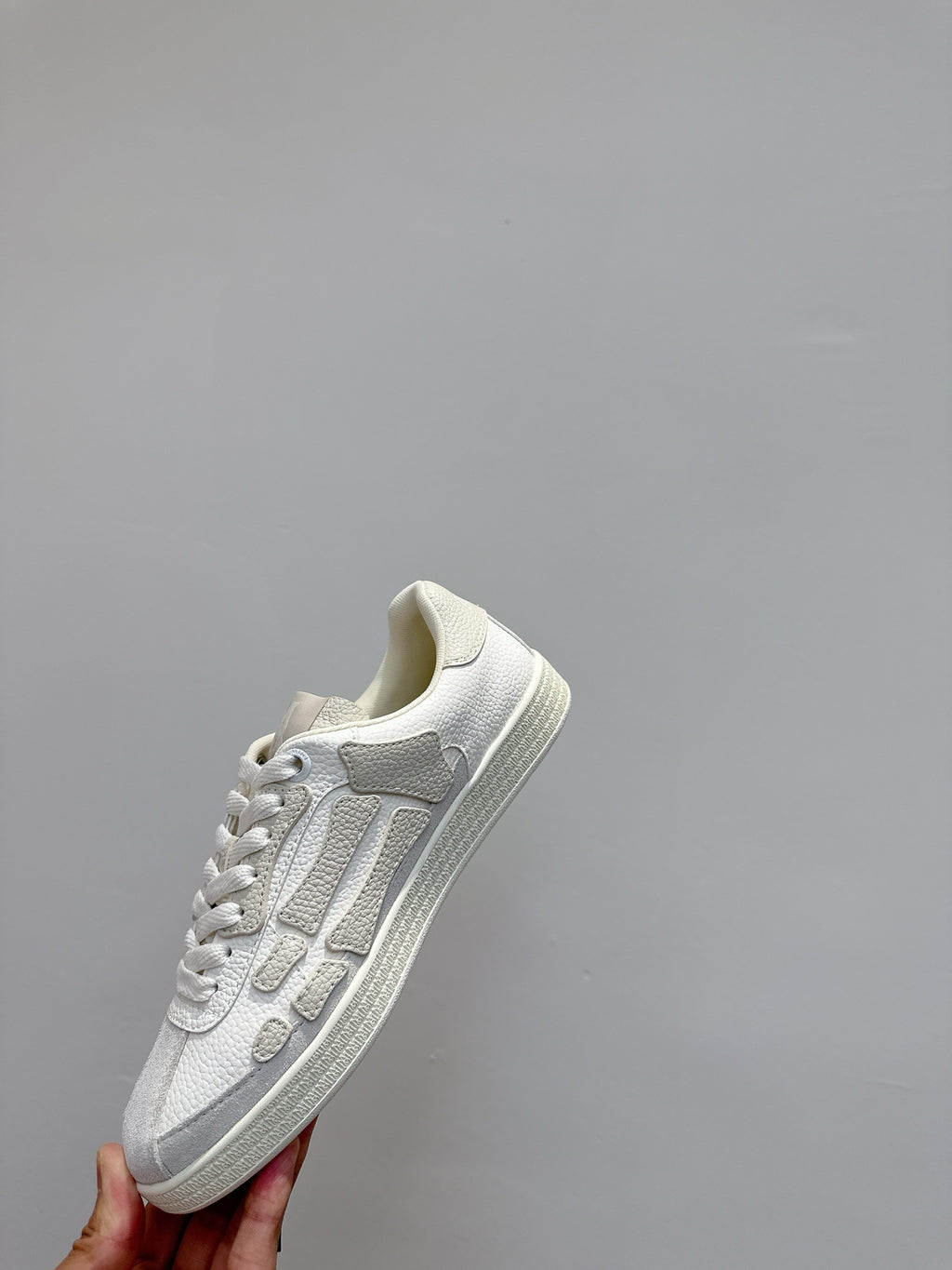 White sneakers held up, showing side profile with raised stripe detail