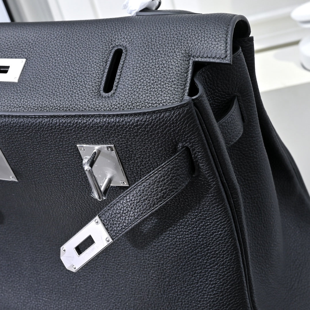 Black pebbled leather handbag detail with silver hardware plaques and cutout handle