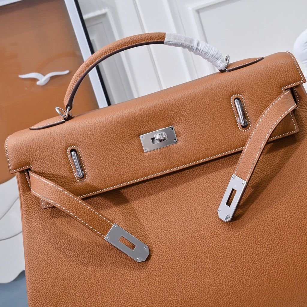 Hermes leather bag in tan-brown with front flap, metal lock plate, and side handle loops.