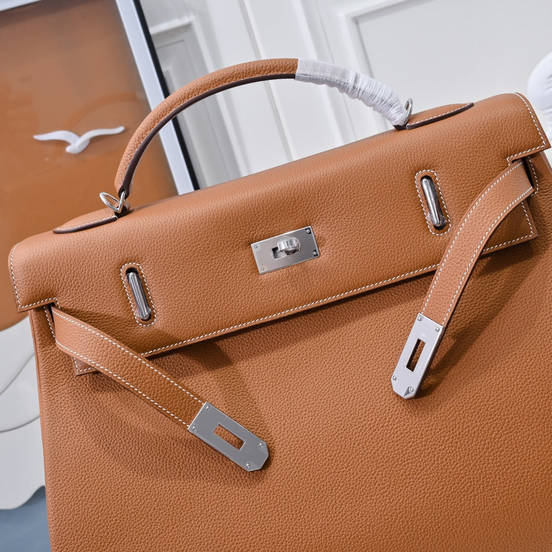 Hermes leather bag in tan-brown with front flap, metal lock plate, and side handle loops.