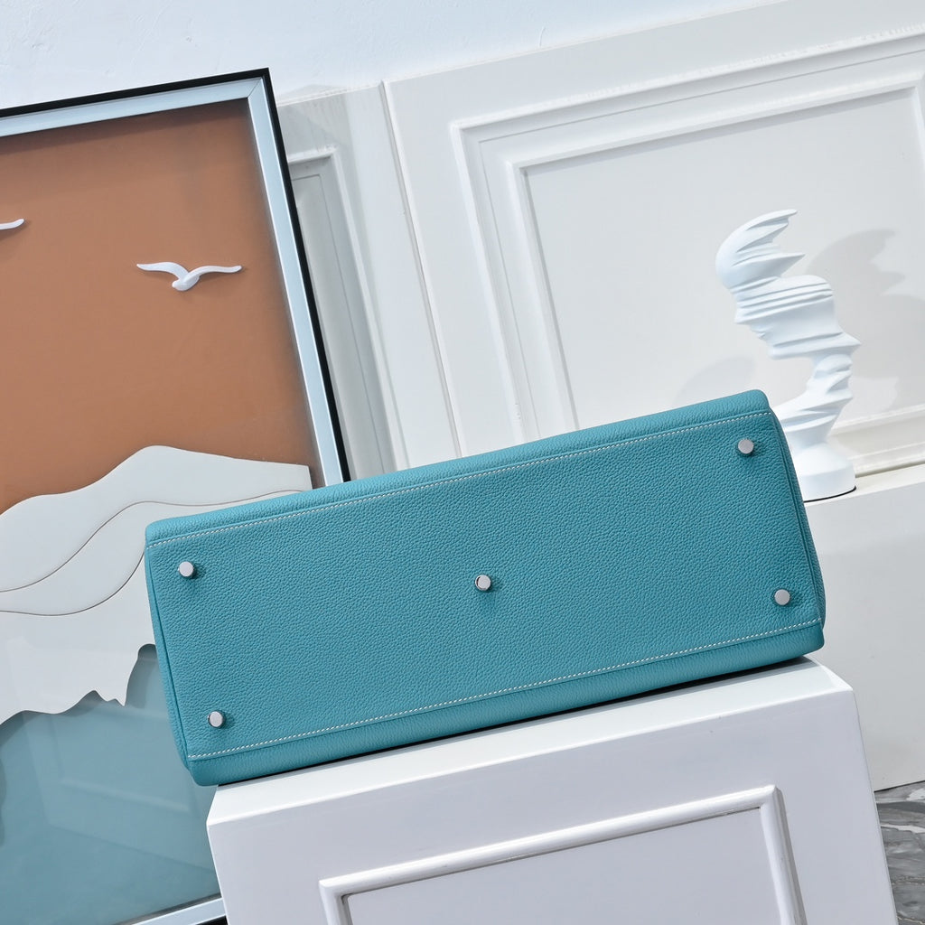 Turquoise leather handbag with long front flap, metal feet studs at corners