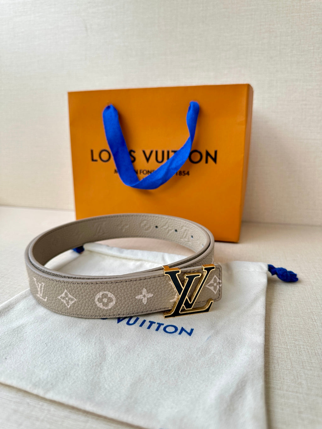 Gray monogram belt with LV buckle and blue tie, laid on white pouch