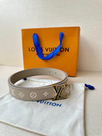 Gray monogram belt with LV buckle and blue tie, laid on white pouch