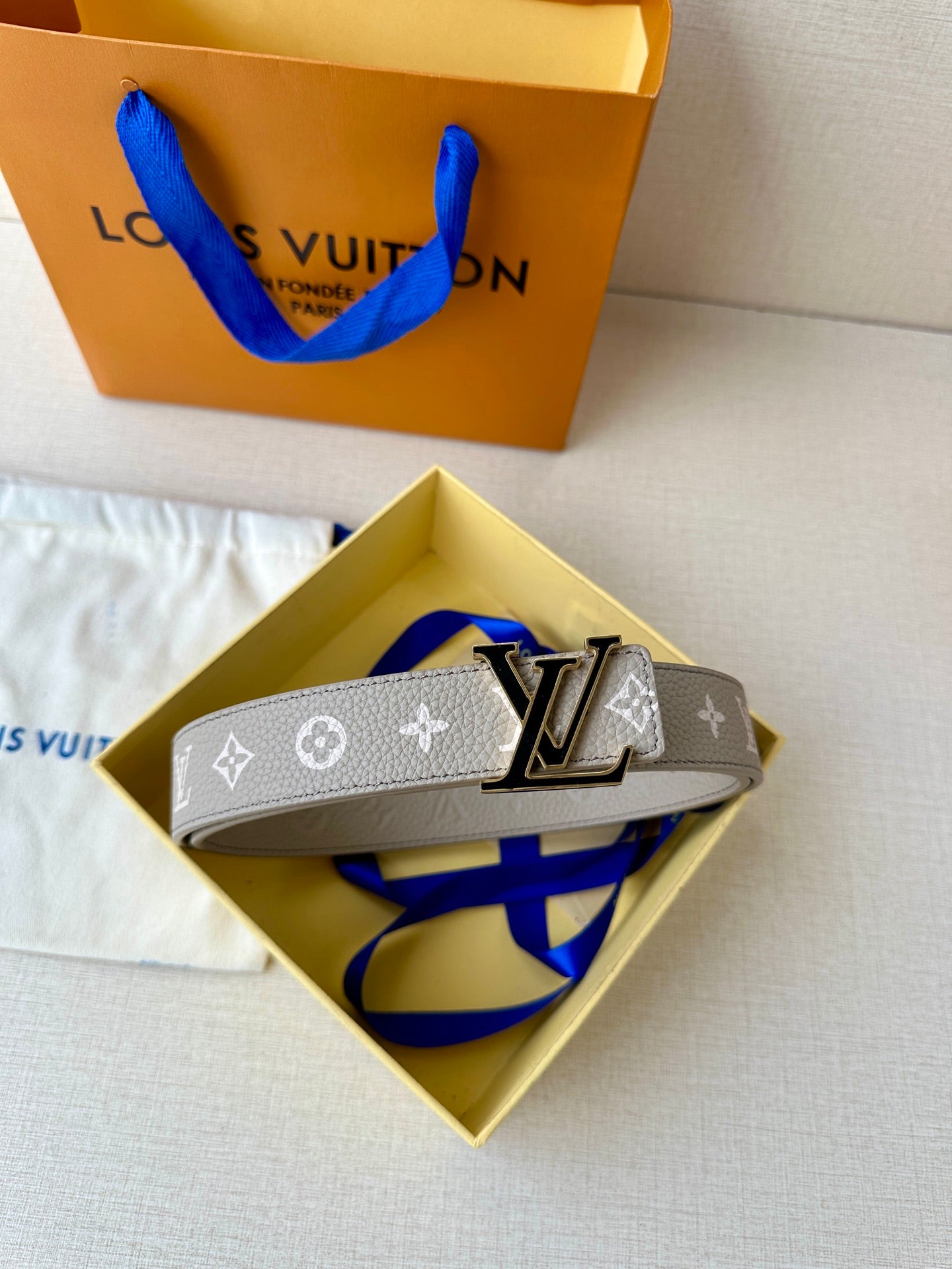 Gray monogram belt in box with LV buckle and blue tie accent