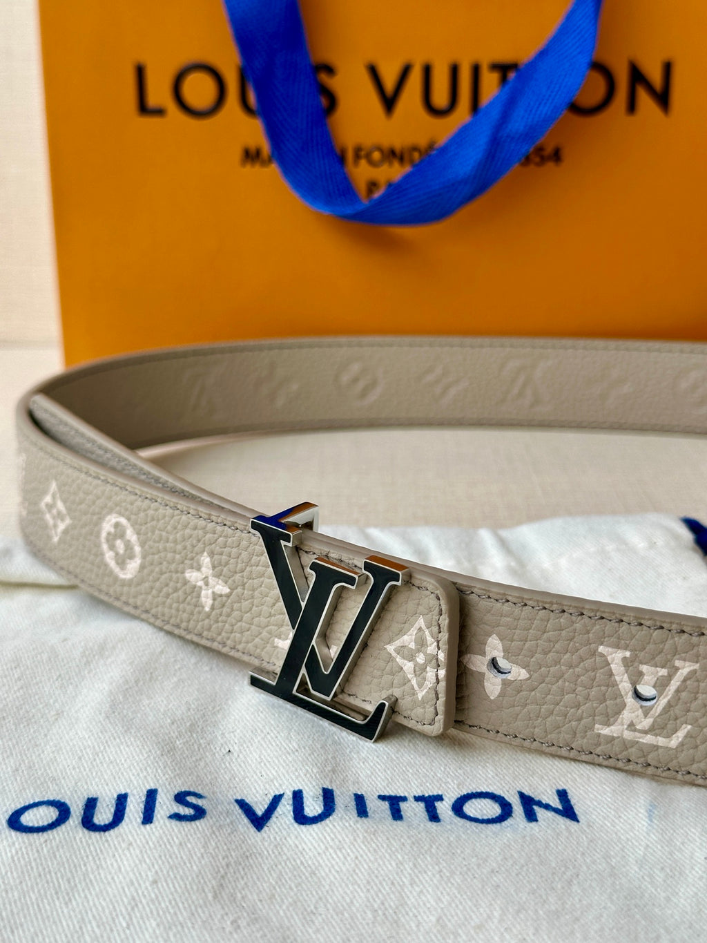 Gray monogram belt close-up of LV buckle on stitched strap, blue edge