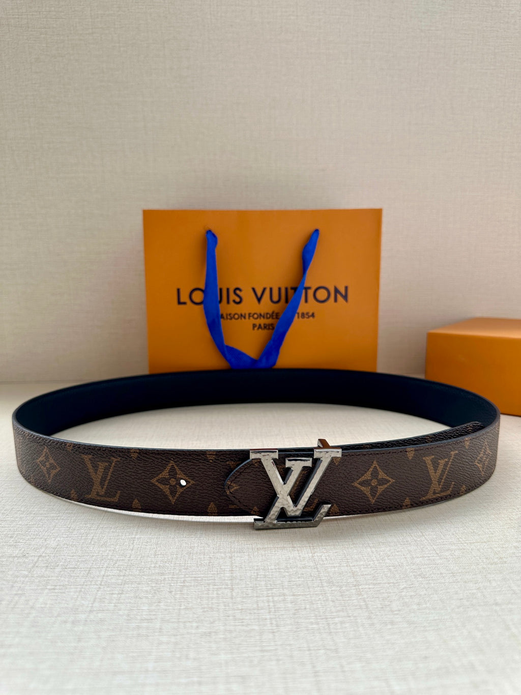 Brown monogram belt with silver-tone LV buckle and blue tassel accents.