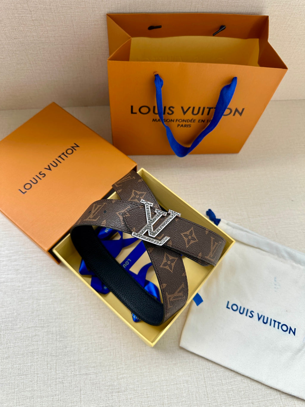 Monogram belt with silver-tone LV buckle, styled with blue accessories and dust bags.