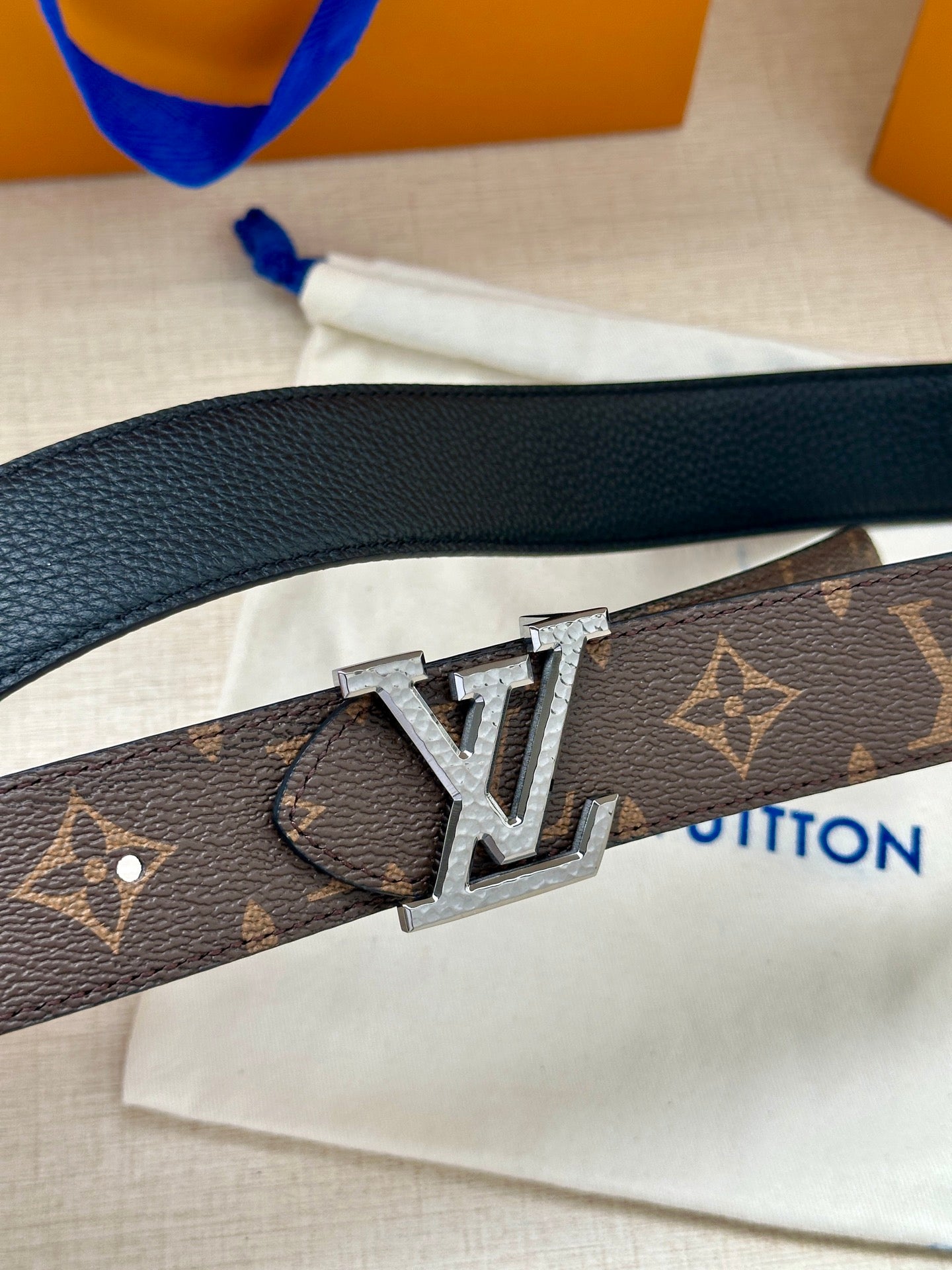 Monogram belt close-up with silver-tone LV buckle on dark strap.