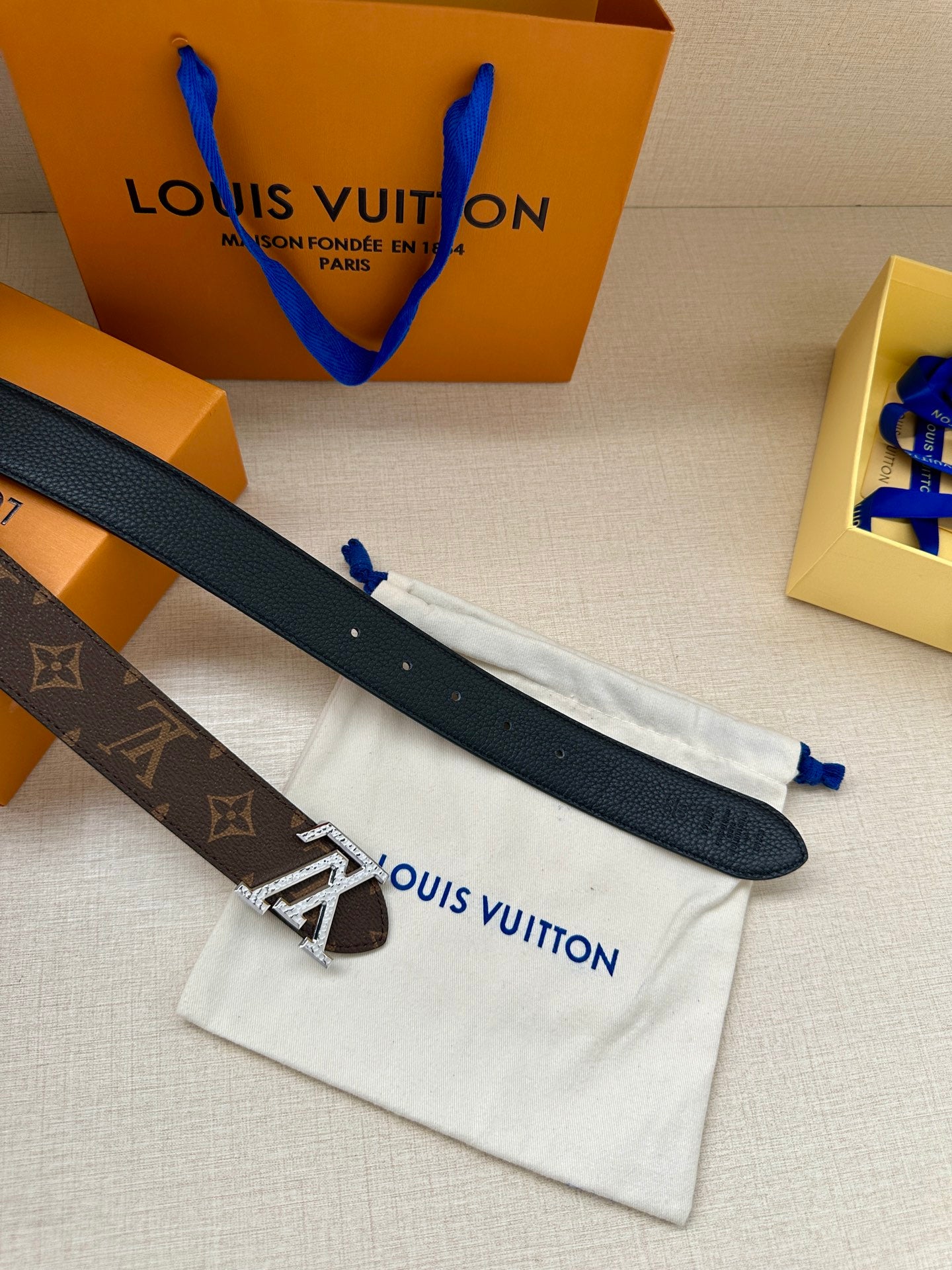Navy leather belt with silver buckle, laid on white dust bag with blue ties.