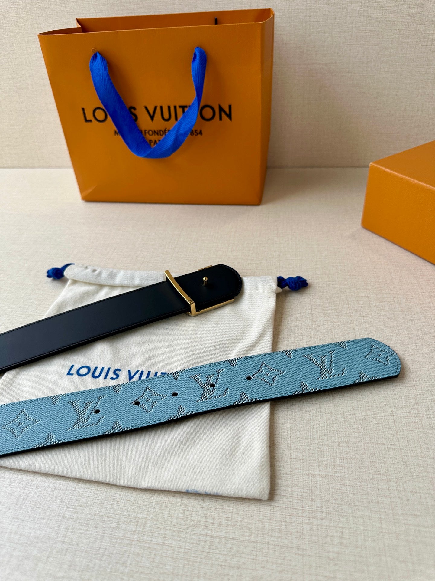 Louis Vuitton belt flat on dust bag, blue monogram strap with gold LV buckle and black edge.