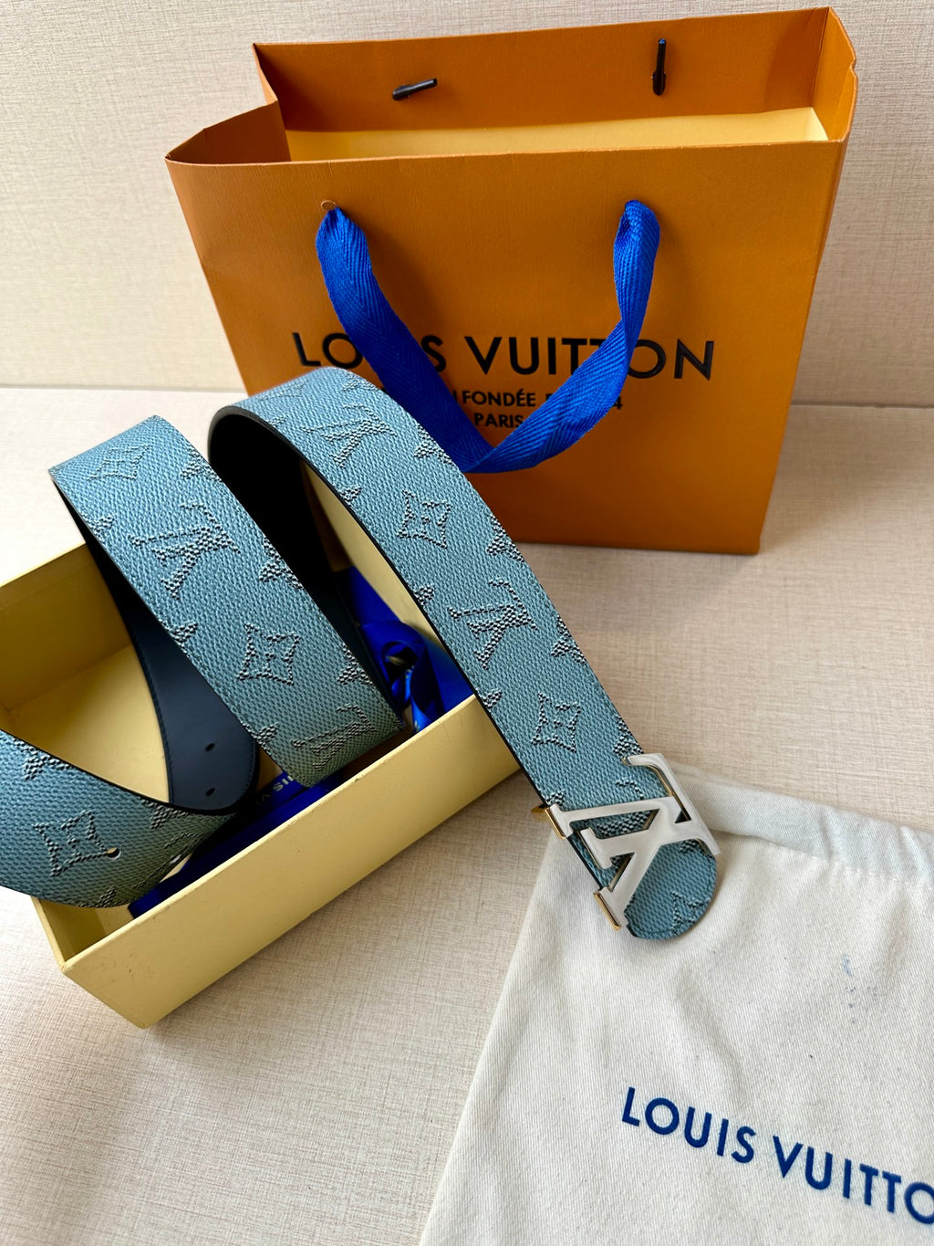 Louis Vuitton belt set with blue monogram strap, gold LV buckle, and black underside on bag.