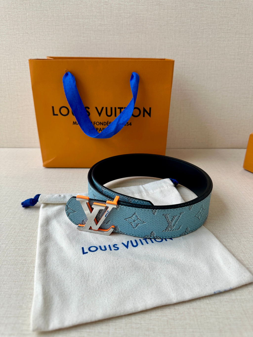 Light blue monogram belt on white dust bag, with LV logo buckle