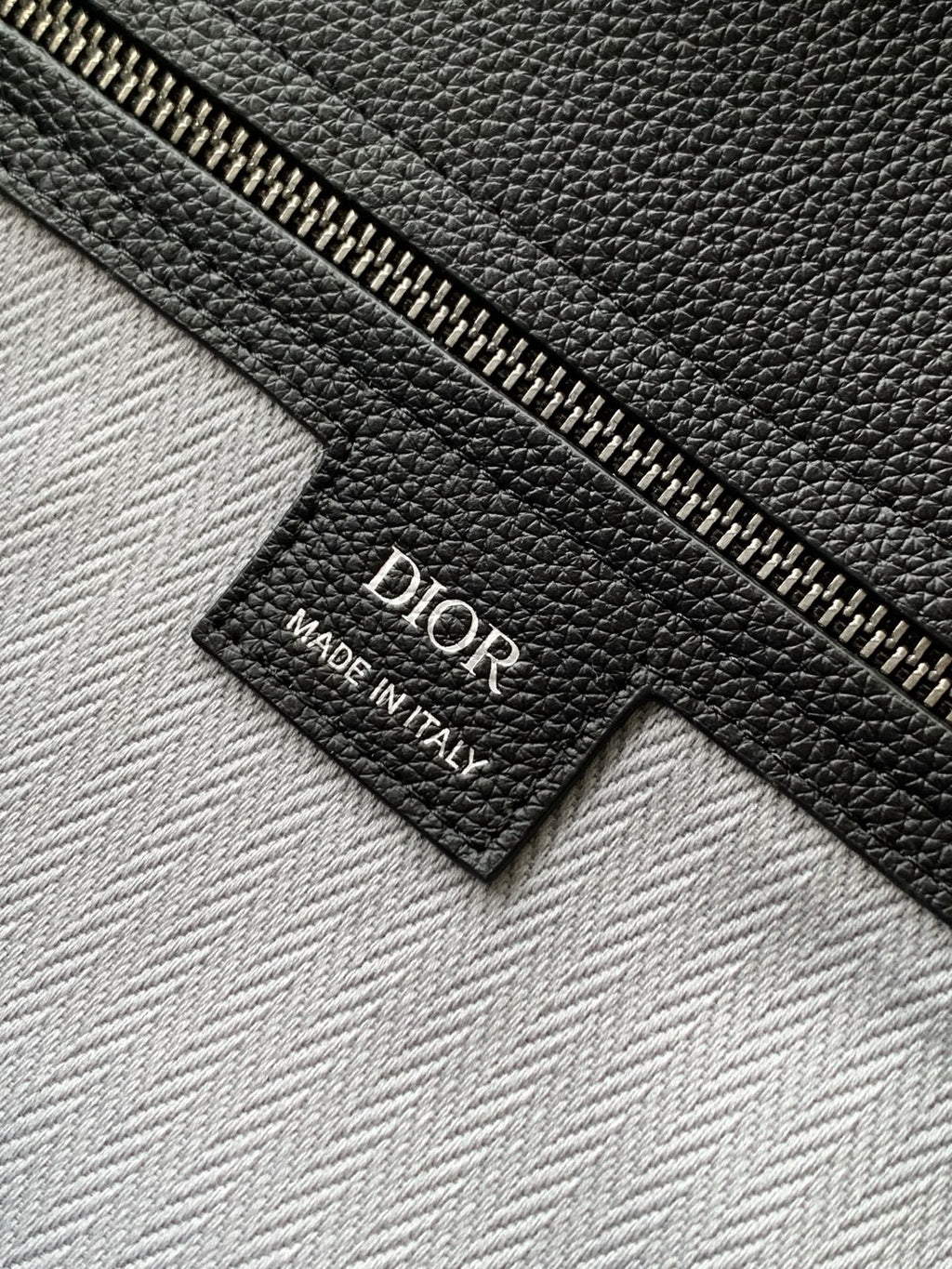 Dior men’s leather bag tag reading “Dior Made in Italy”