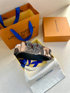 Camo designer belt with wide strap and silver-toned ornate buckle over dust bag