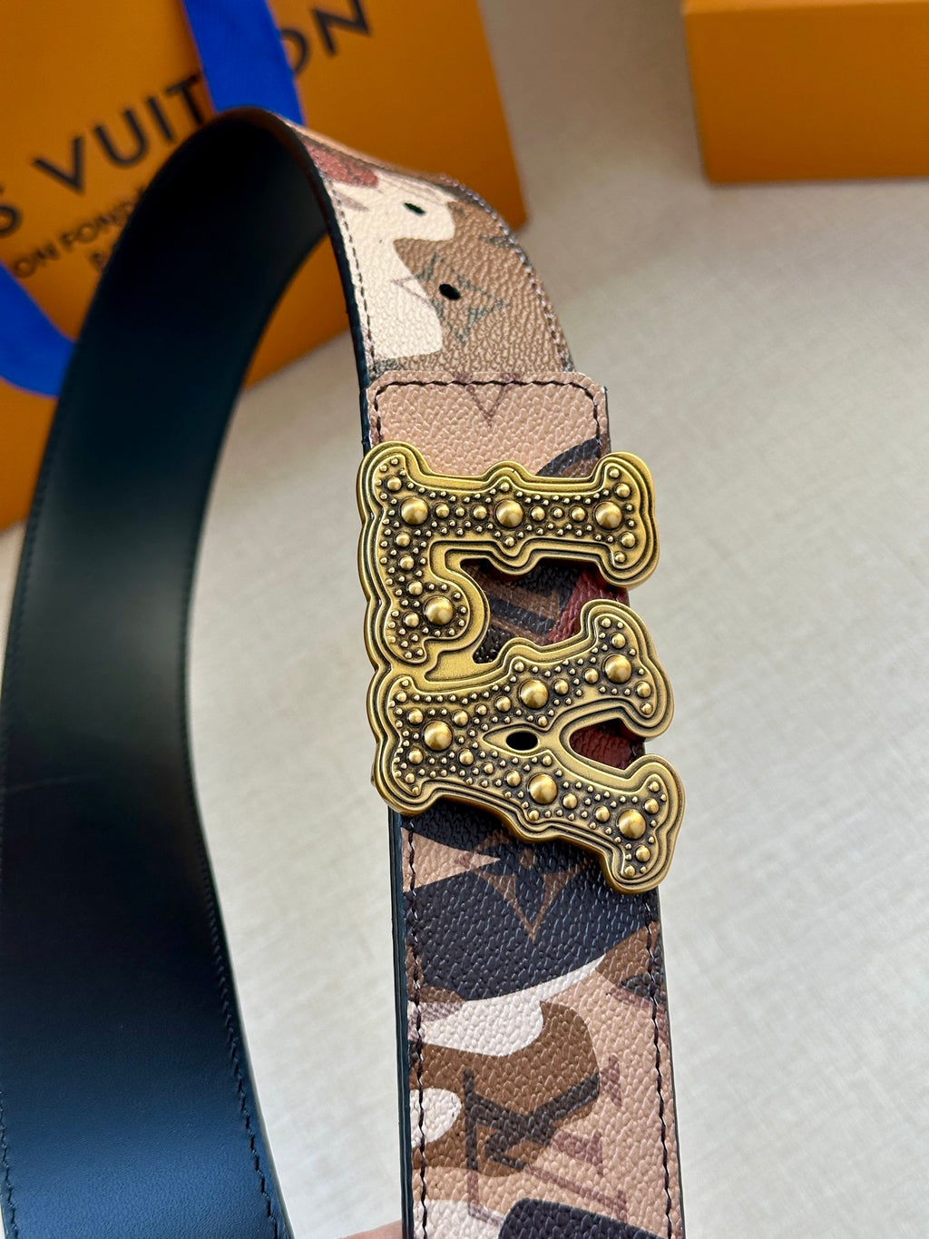 Camo belt strap with gold-tone buckle, stud detailing on patterned leather panel