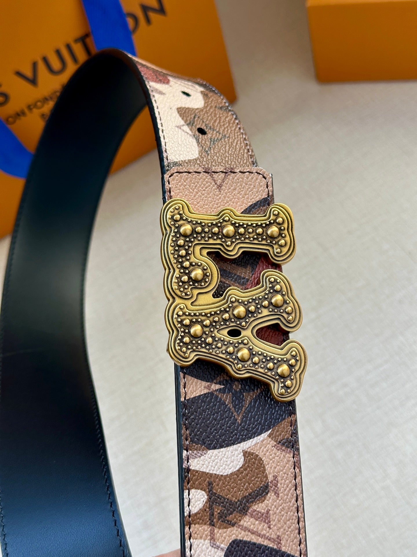 Camo belt strap with gold-tone buckle, stud detailing on patterned leather panel