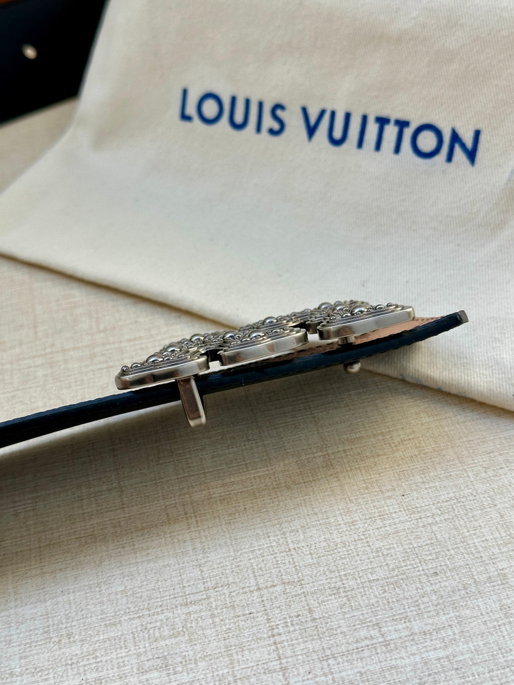 Belt buckle detail with silver-toned hardware on dark strap, resting on dust bag