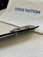 Belt buckle detail with silver-toned hardware on dark strap, resting on dust bag