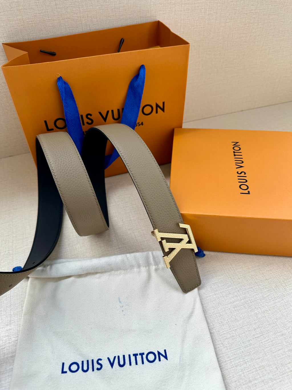 Louis Vuitton belt close-up: beige strap with gold LV buckle, paired with dark strap
