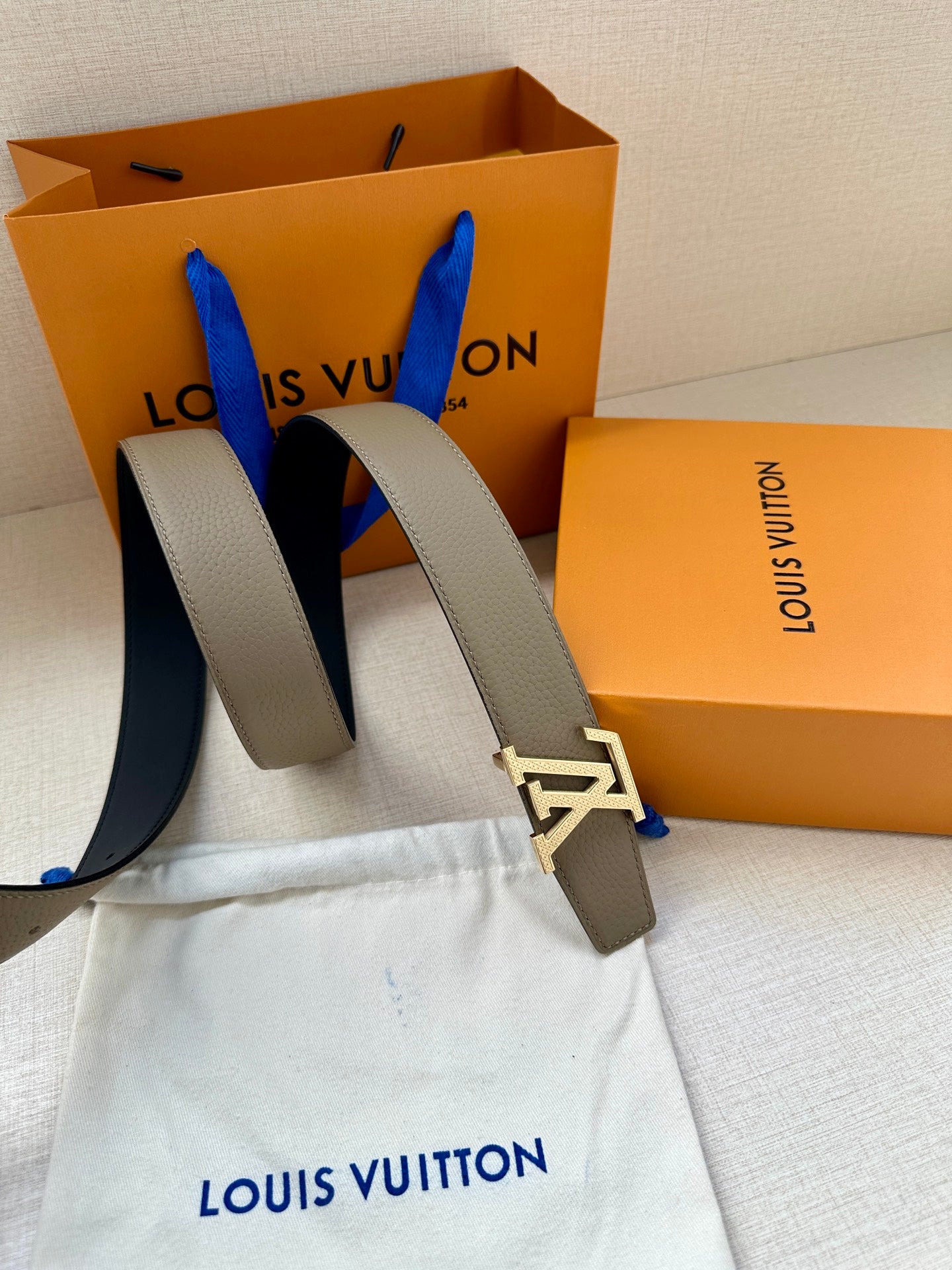 Louis Vuitton belt close-up: beige strap with gold LV buckle, paired with dark strap