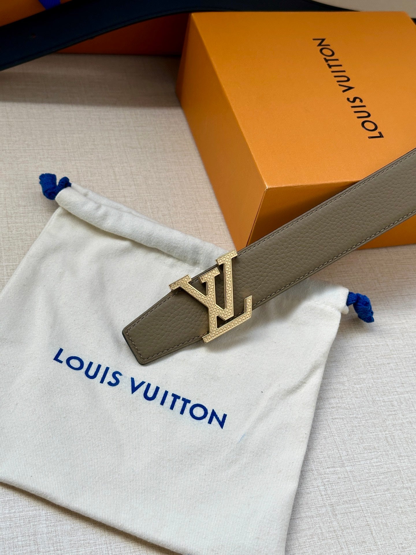 Louis Vuitton belt close-up: beige strap with gold LV buckle on white dust bag