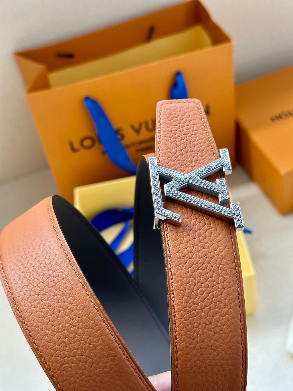 Leather belt with brown textured strap and silver LV buckle, close-up.
