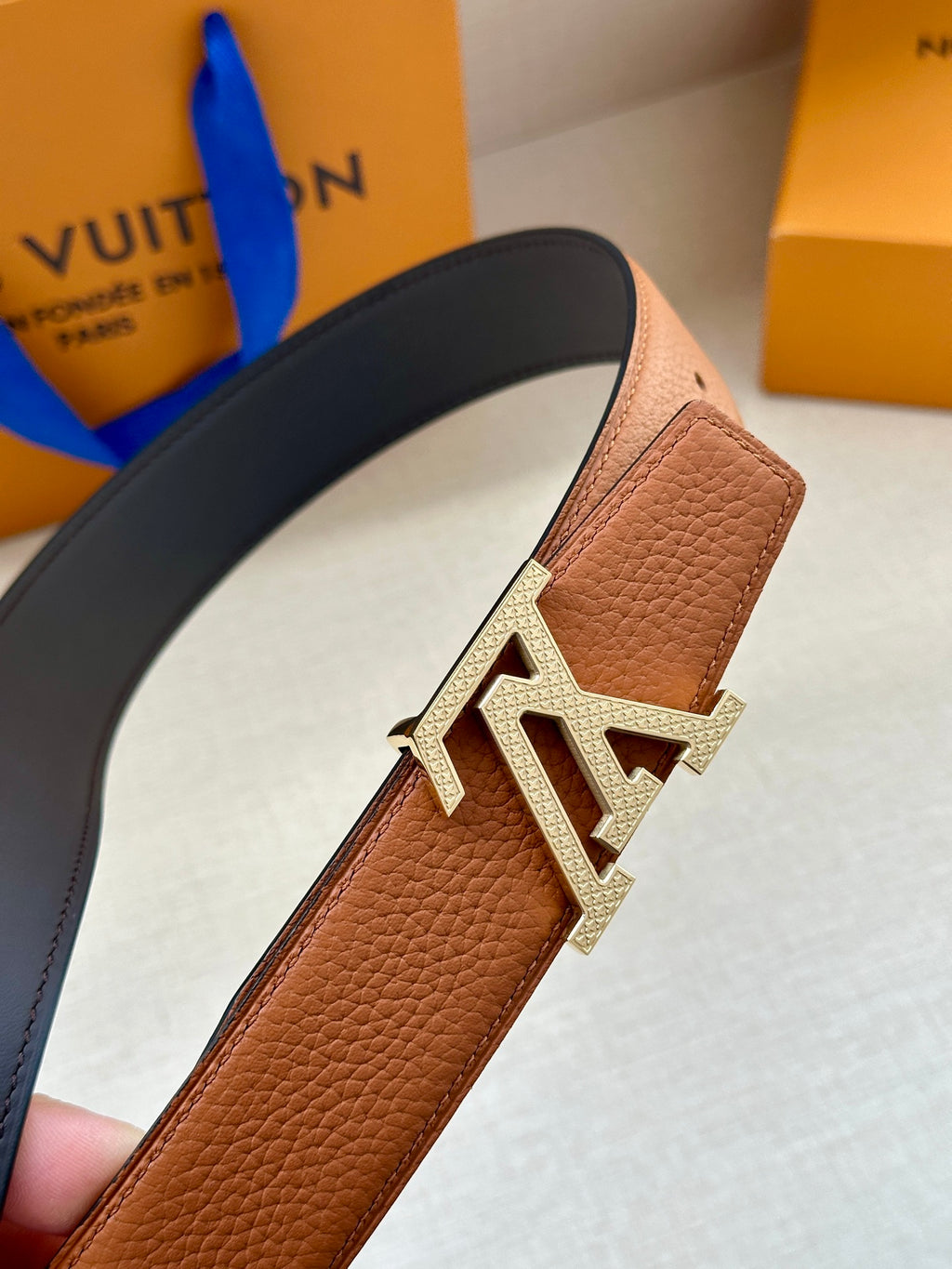 Leather belt, brown textured strap with silver LV buckle on dark back.
