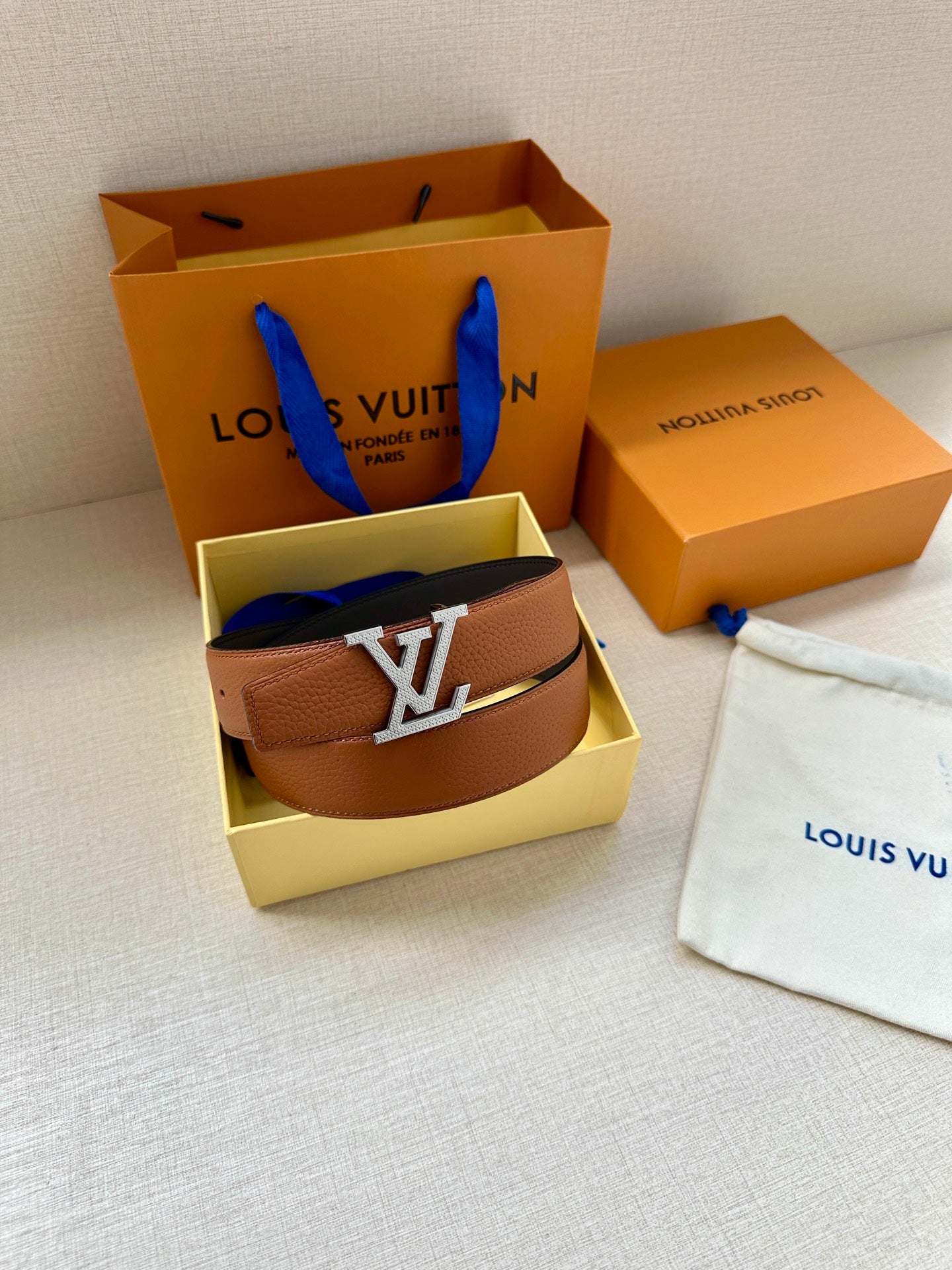 Leather belt with brown strap and silver LV buckle, in open box.