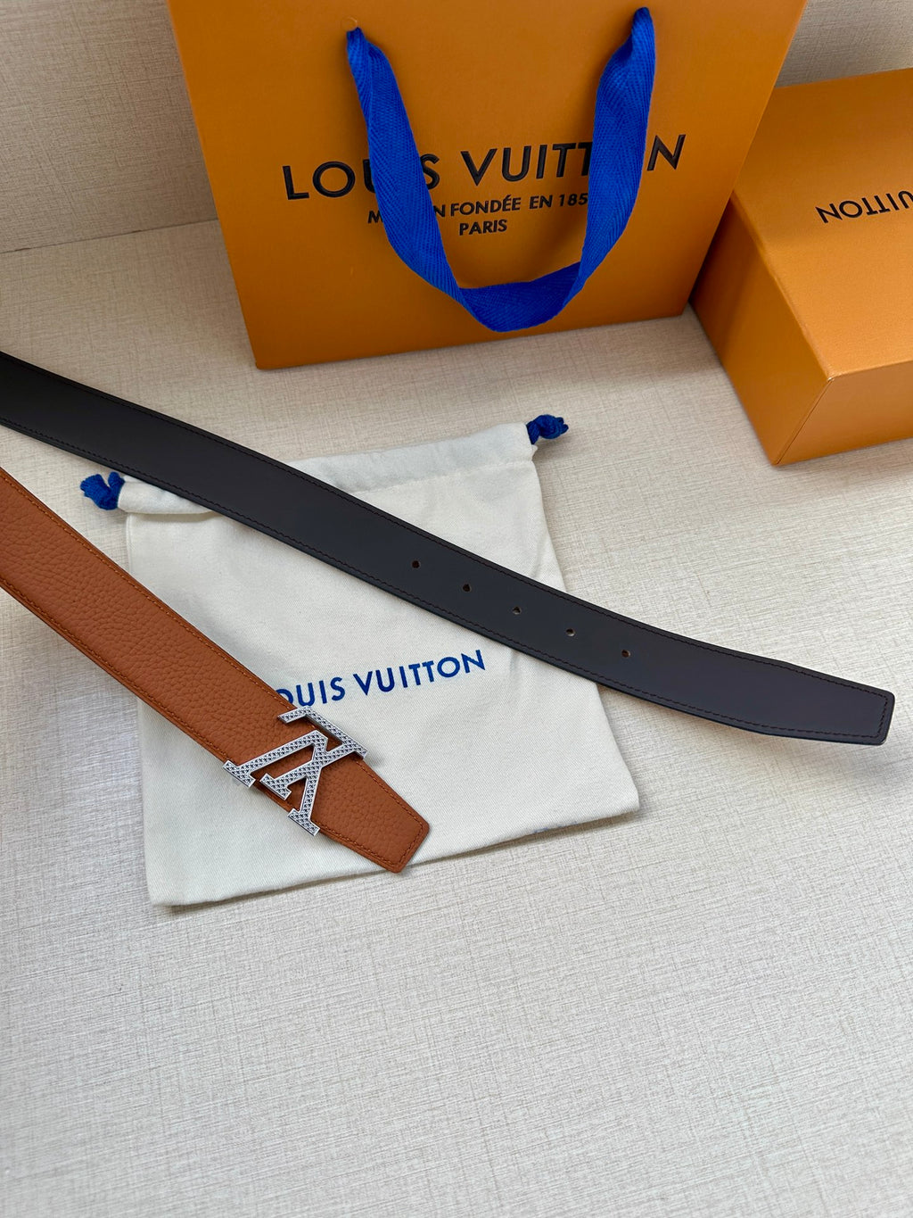 Brown and black belt straps with silver LV buckle, laid on dust bags.
