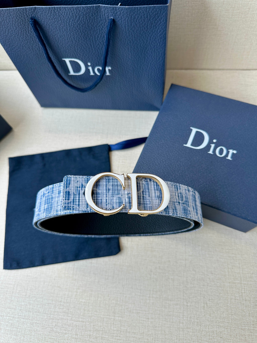Blue patterned belt with silver CD buckle and black underside, styled on cloth.