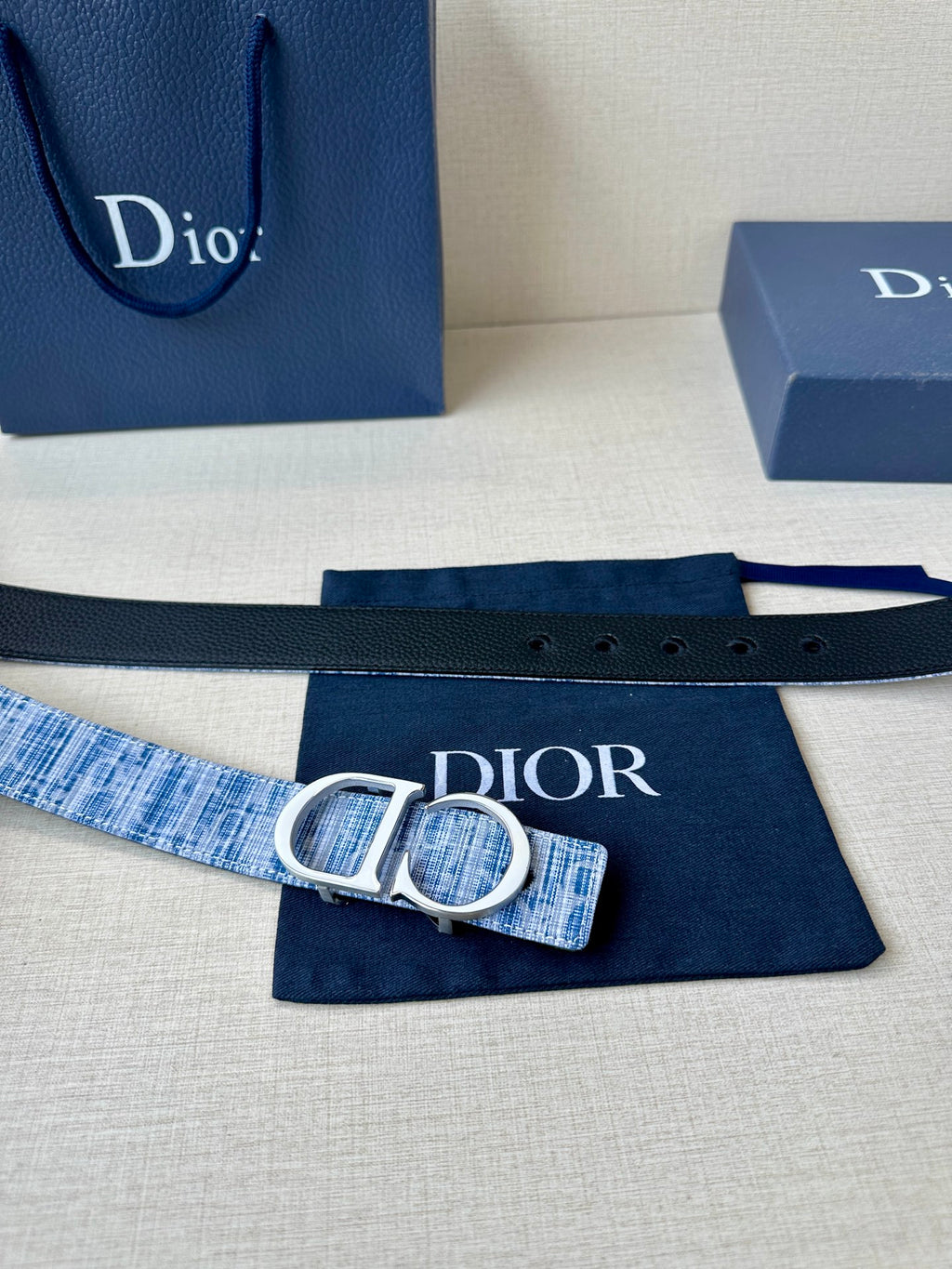 Blue and white woven belt with silver CD buckle, laid flat on navy cloth.