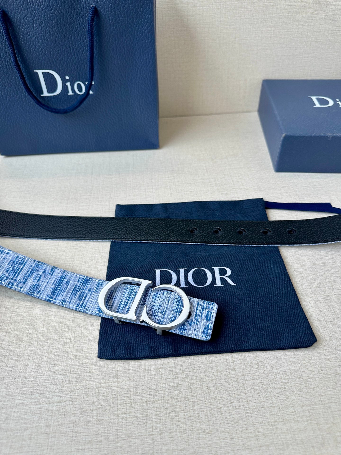 Blue and white woven belt with silver CD buckle, laid flat on navy cloth.