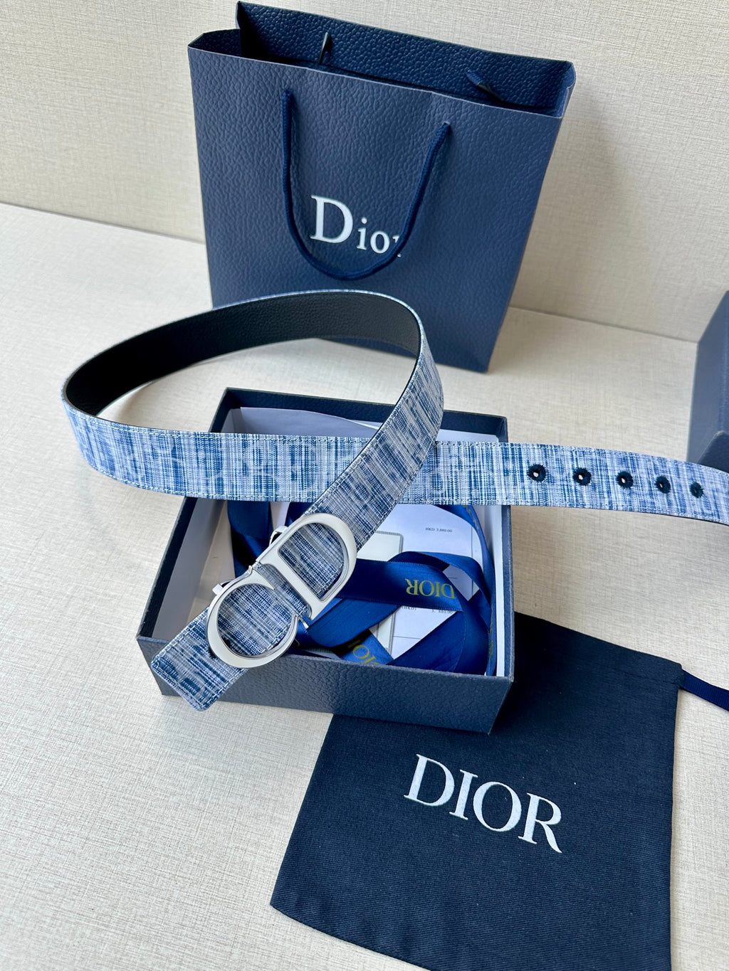 Blue patterned belt with silver CD buckle, folded inside a box with pouch.