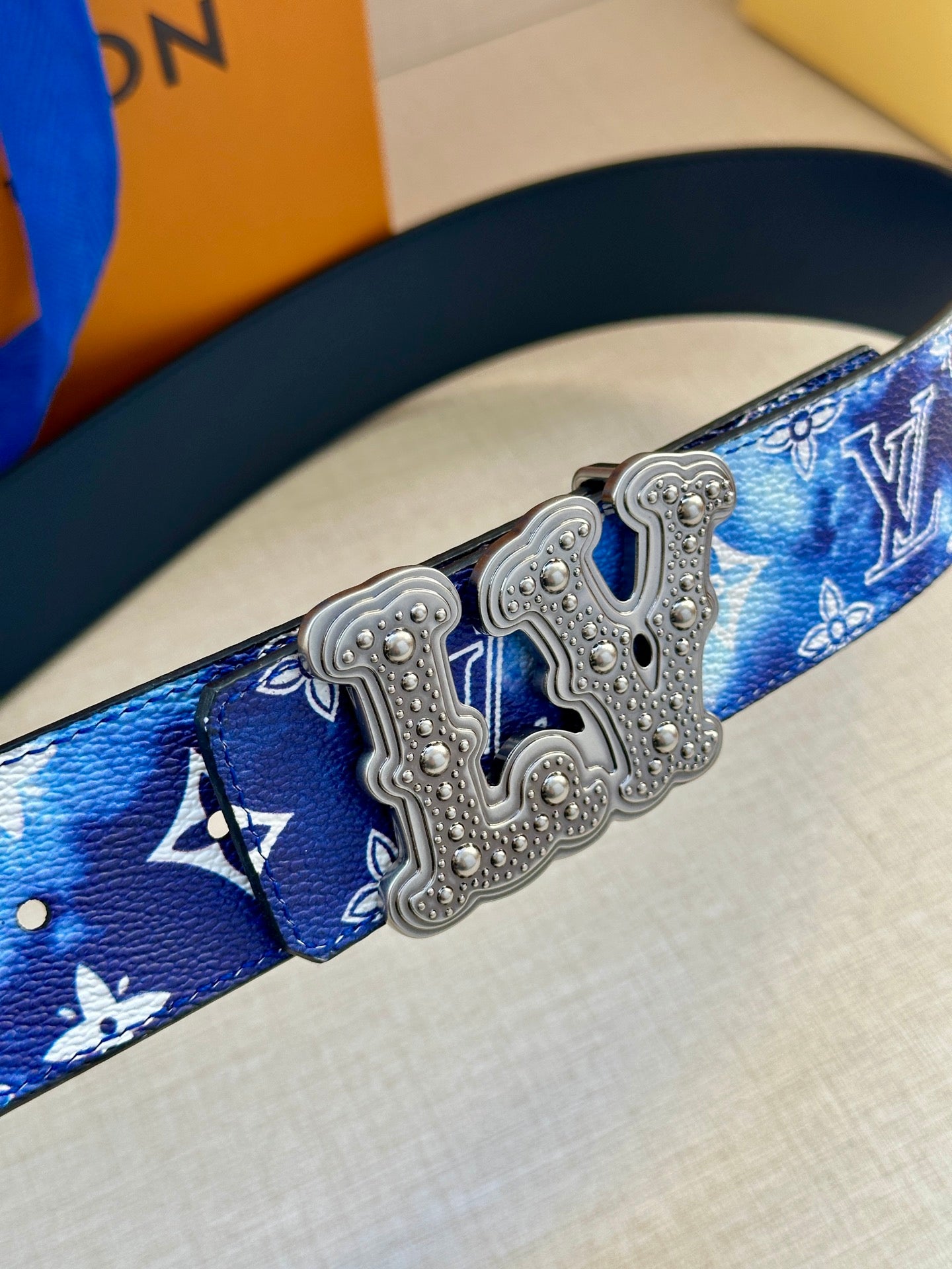 Louis Vuitton belt close-up: blue monogram strap with silver-tone ornate buckle center.