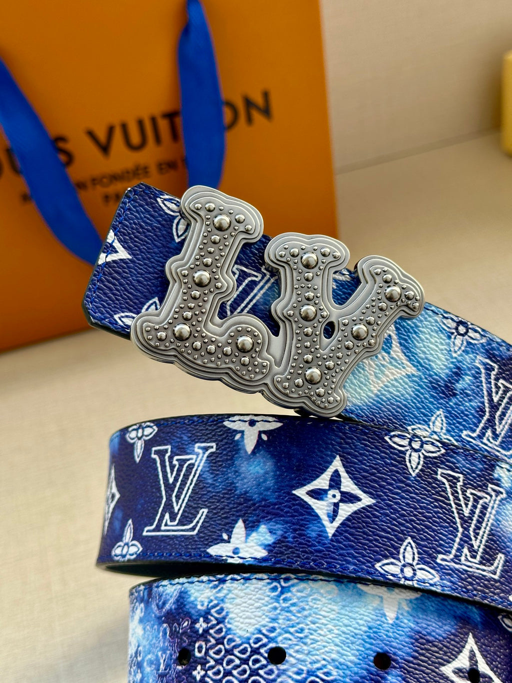 Louis Vuitton belt detail: blue monogram strap with large silver-tone ornate buckle.