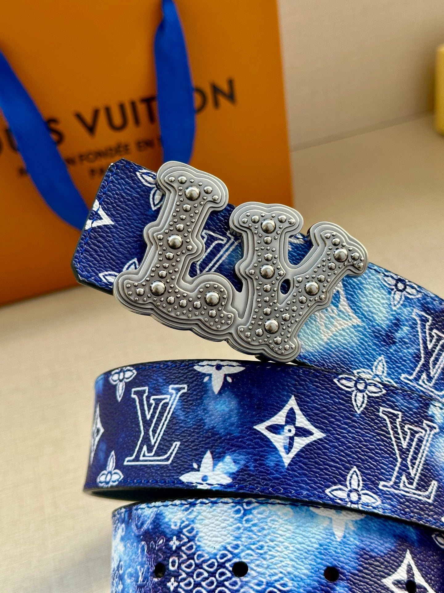Louis Vuitton belt detail: blue monogram strap with large silver-tone ornate buckle.