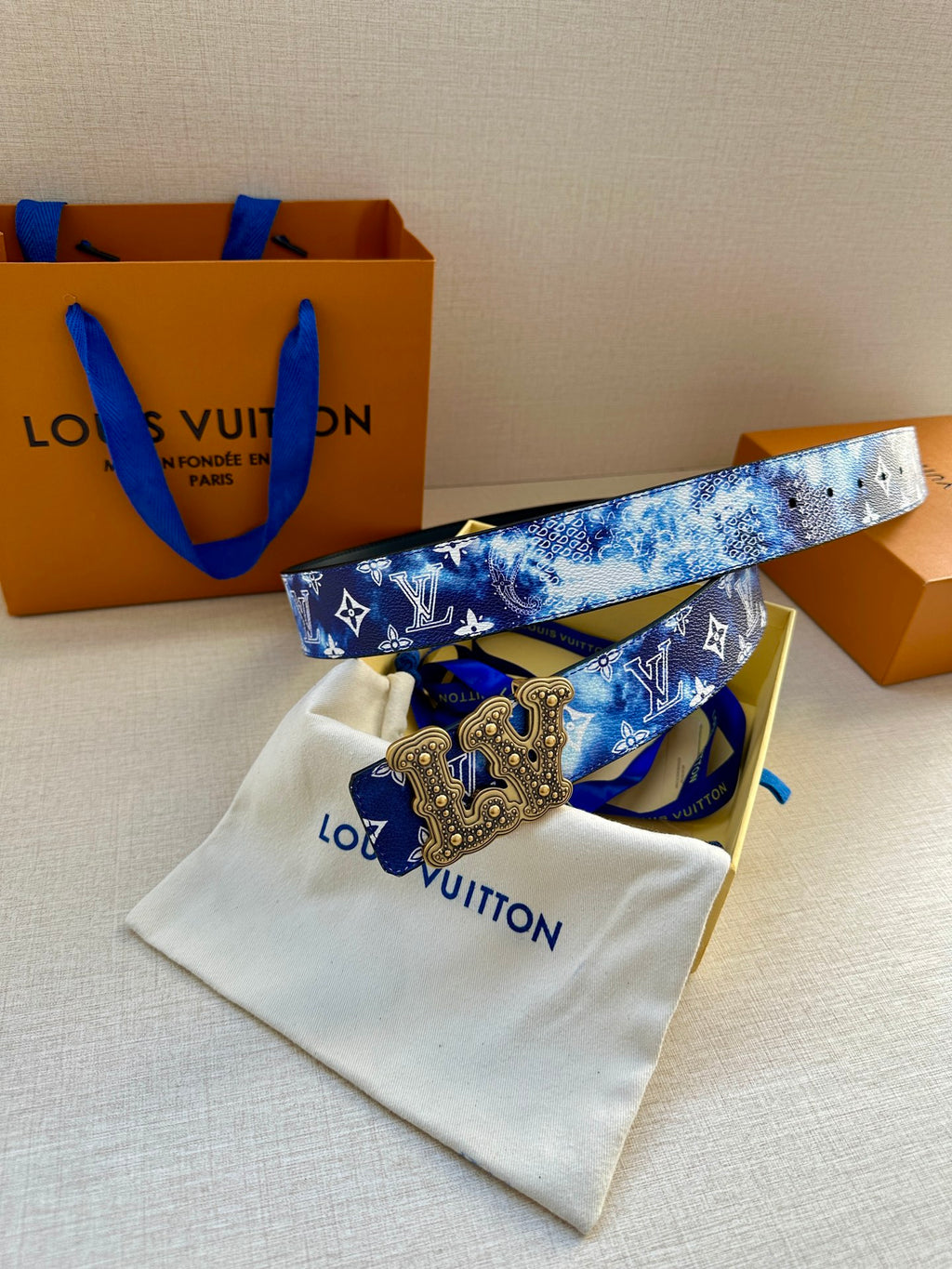 Louis Vuitton belt with blue monogram print and gold-tone ornate buckle, strap laid flat.