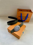 Dark green leather belt with large oval metal buckle, laid over gift box.