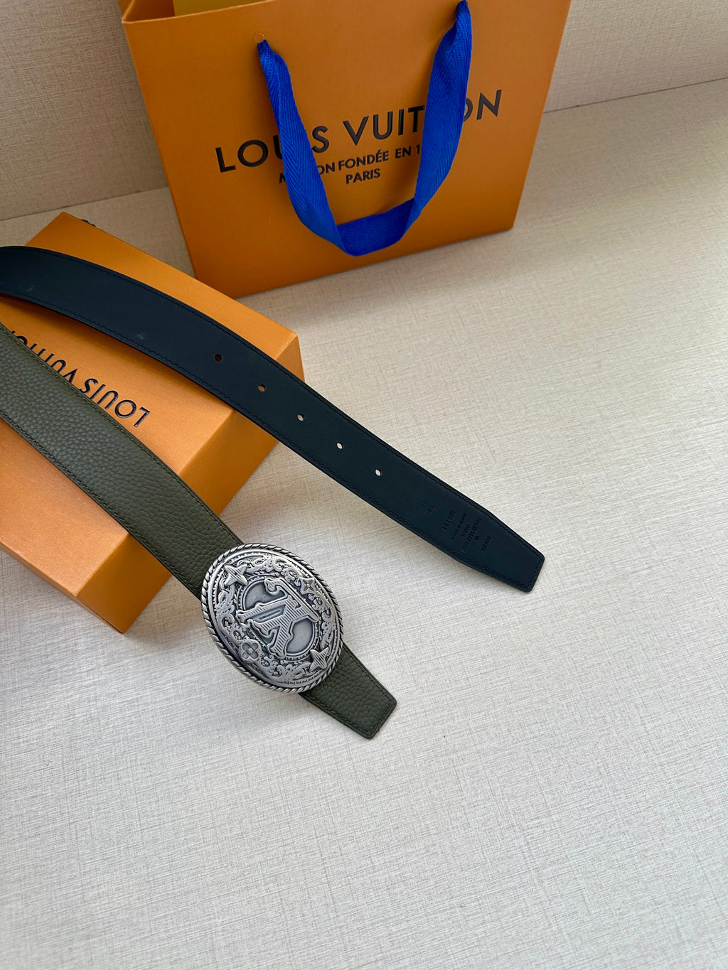 Dark green leather belt with oval logo buckle and long strap ends.