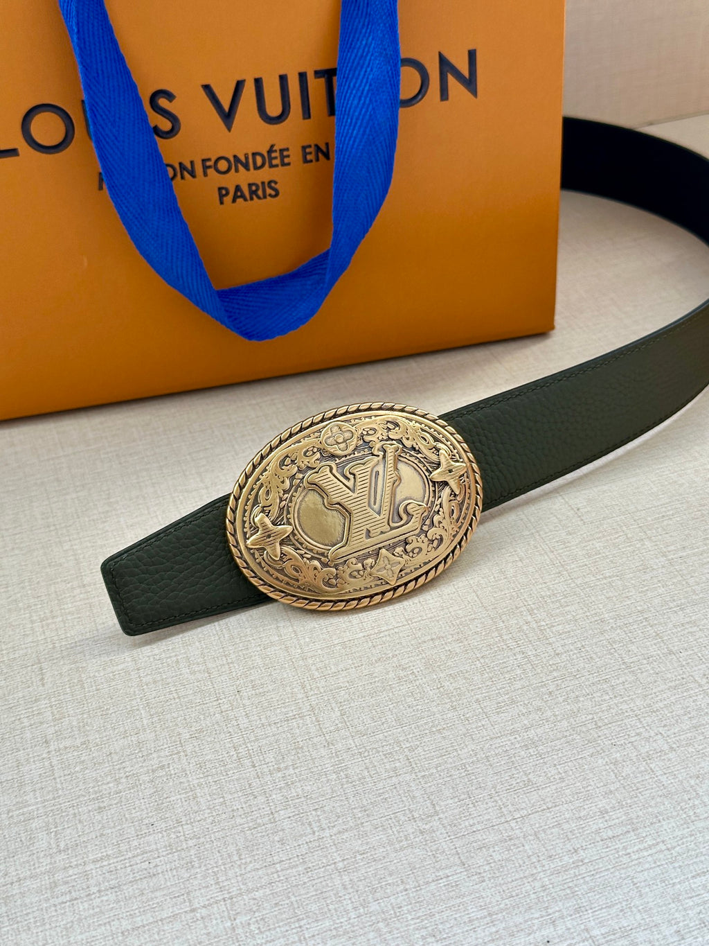 Dark green leather belt with gold-toned ornate oval buckle, close-up detail.