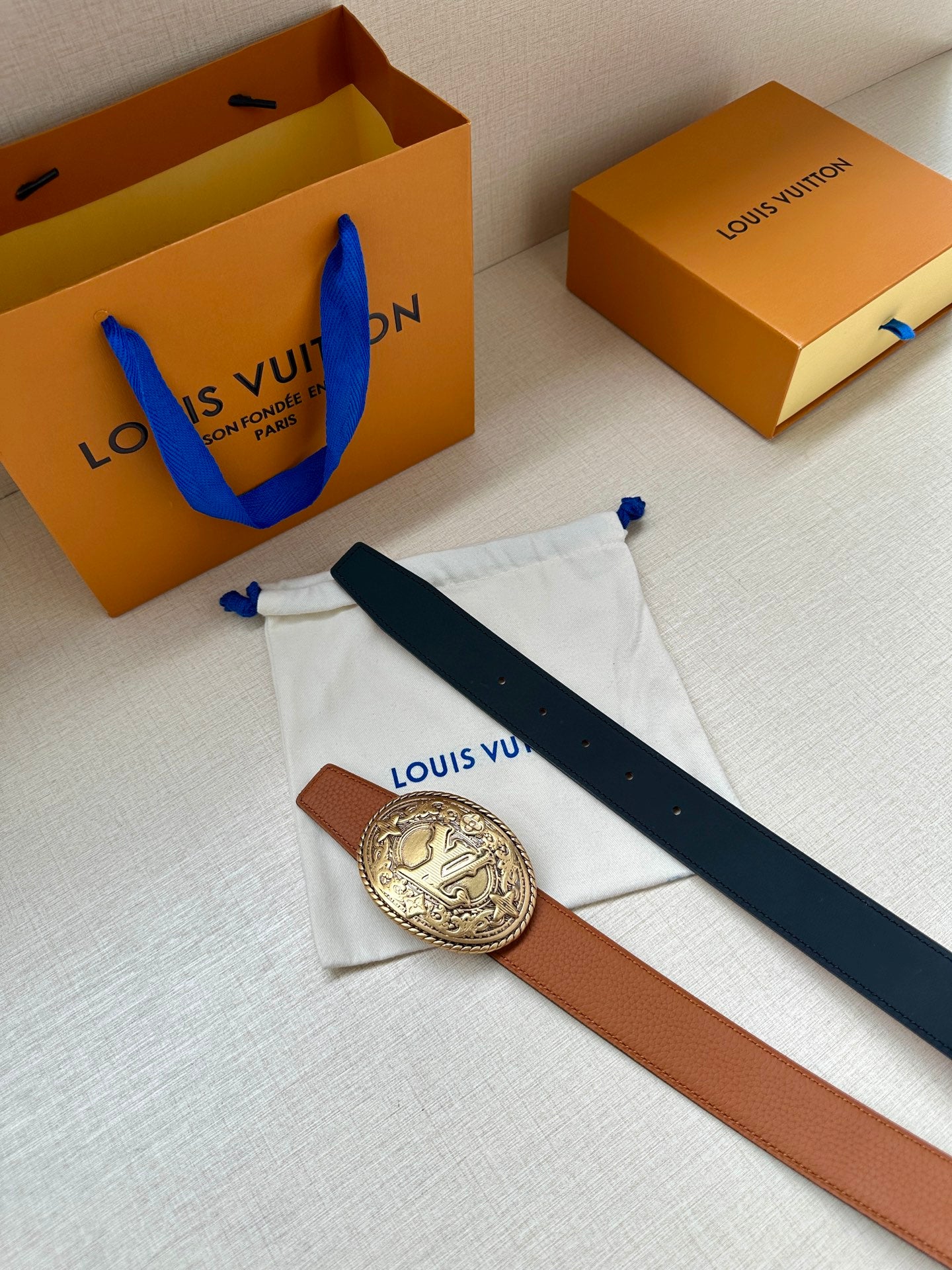 Brown leather belt with silver-tone oval logo buckle and navy belt strap