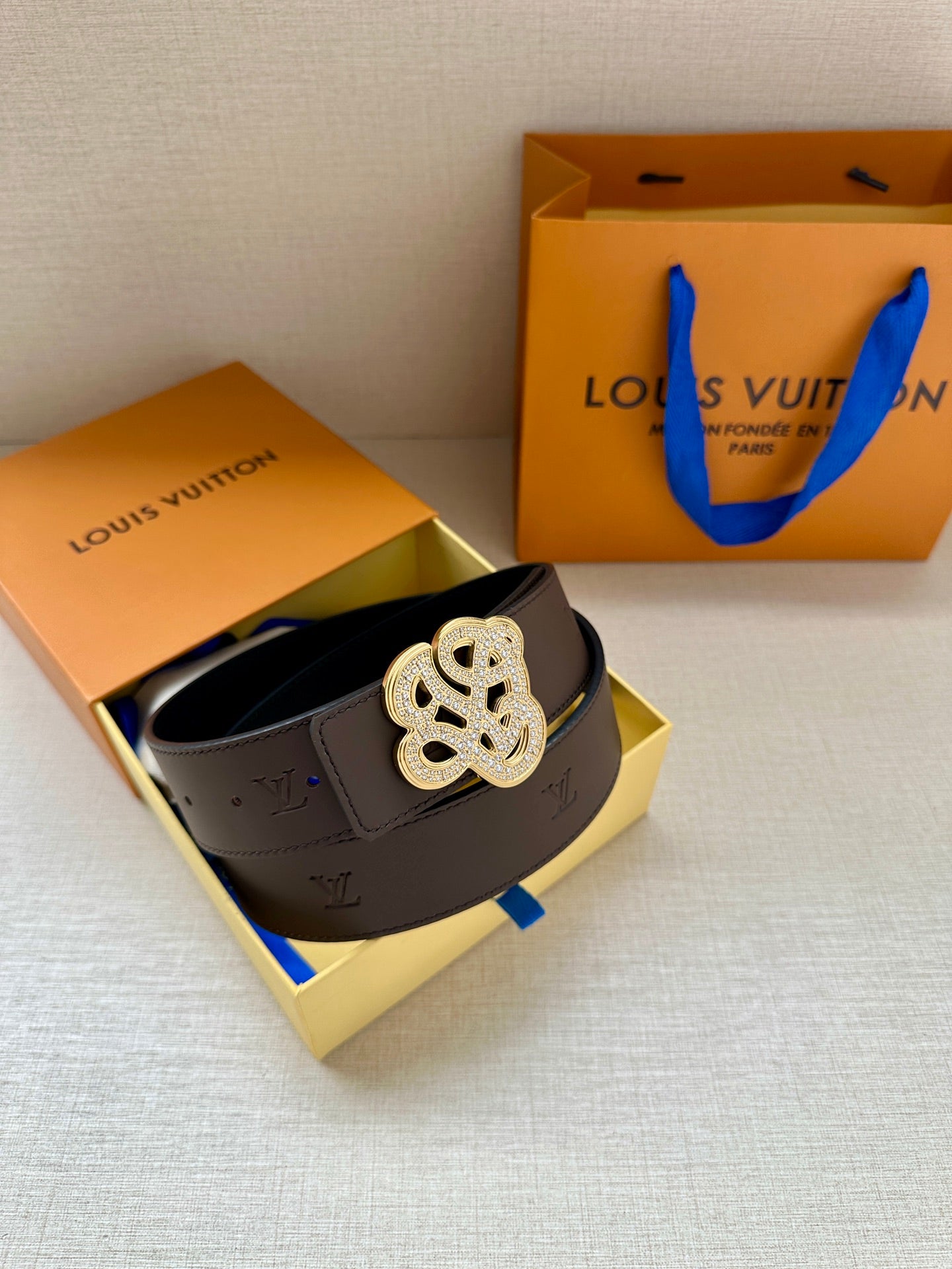 Brown belt with silver monogram buckle inside open box with blue strap ties.