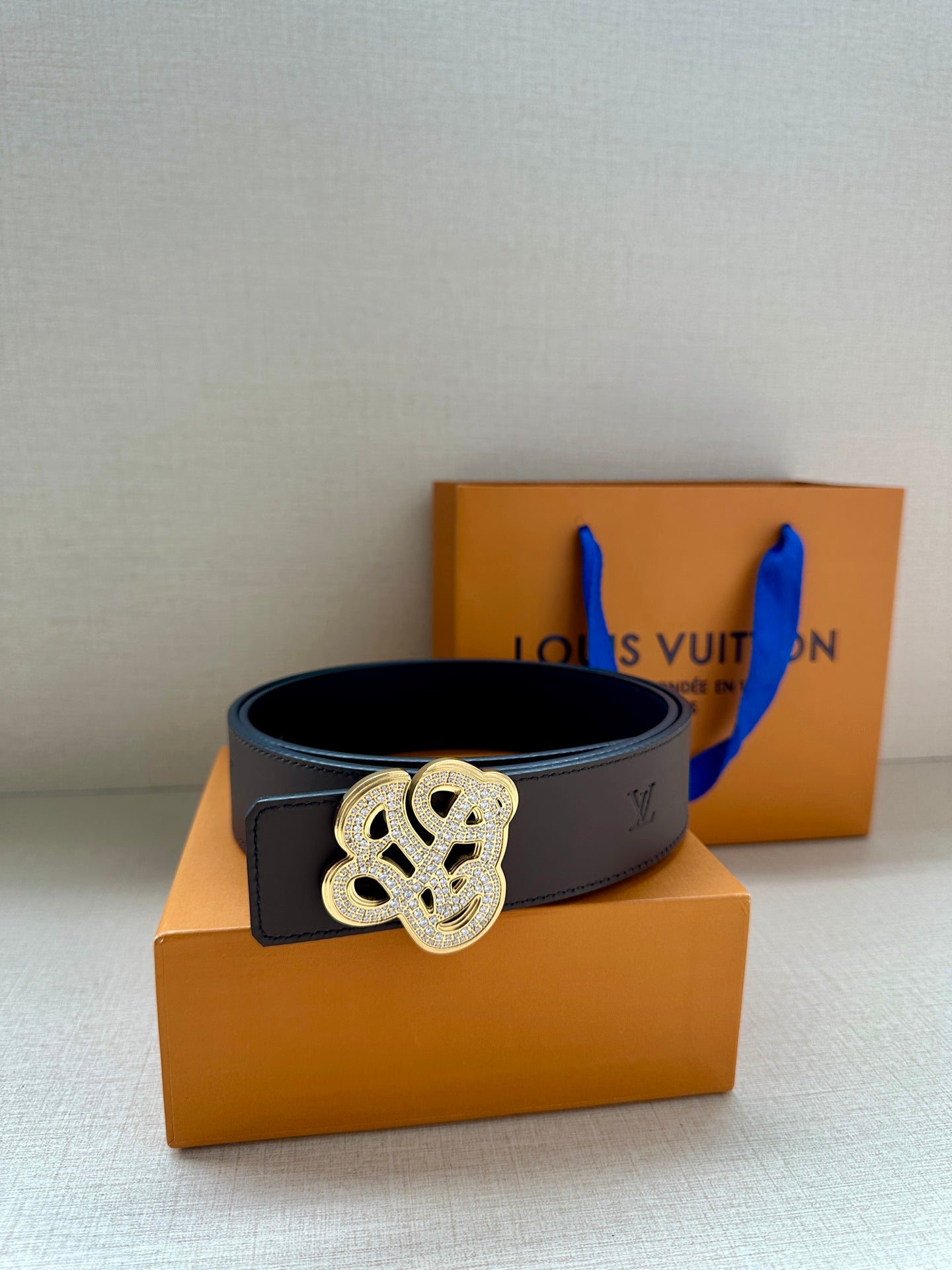 Dark leather belt with gold-toned monogram buckle resting on orange box.