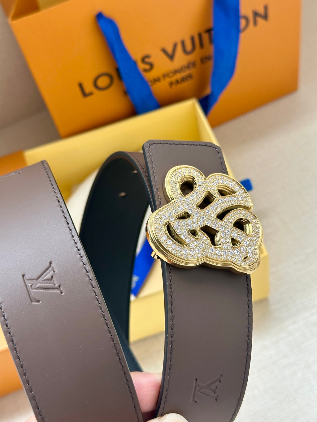 Brown belt strap with gold-toned monogram buckle over dark underside with stitching.