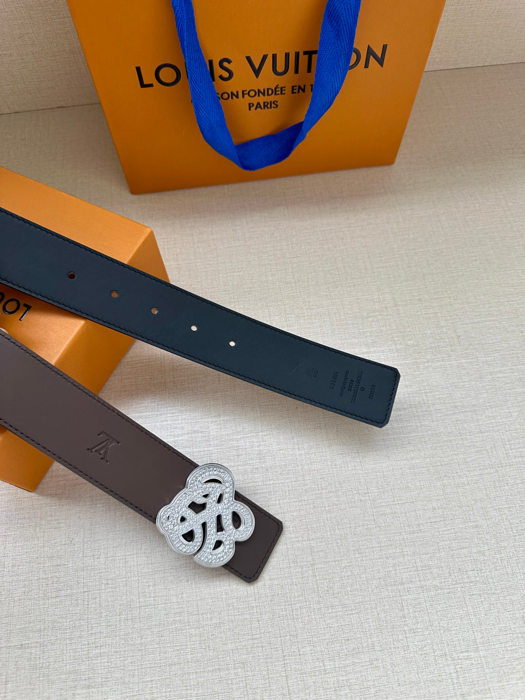 Two-belt view with brown and dark straps, silver monogram buckle at center.